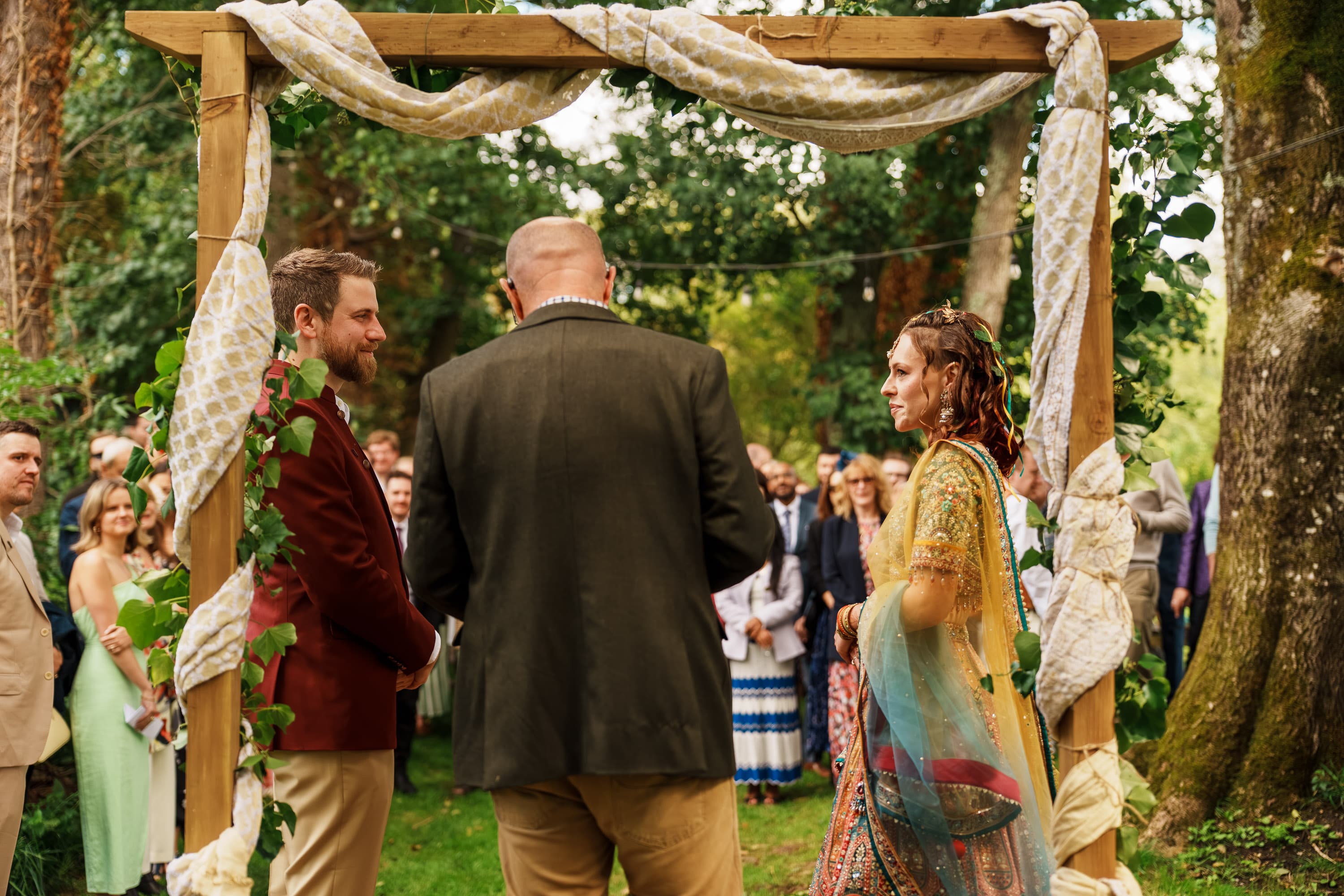 Adam and Sarah facing each other beneath the arch as the ceremony settles into focus.