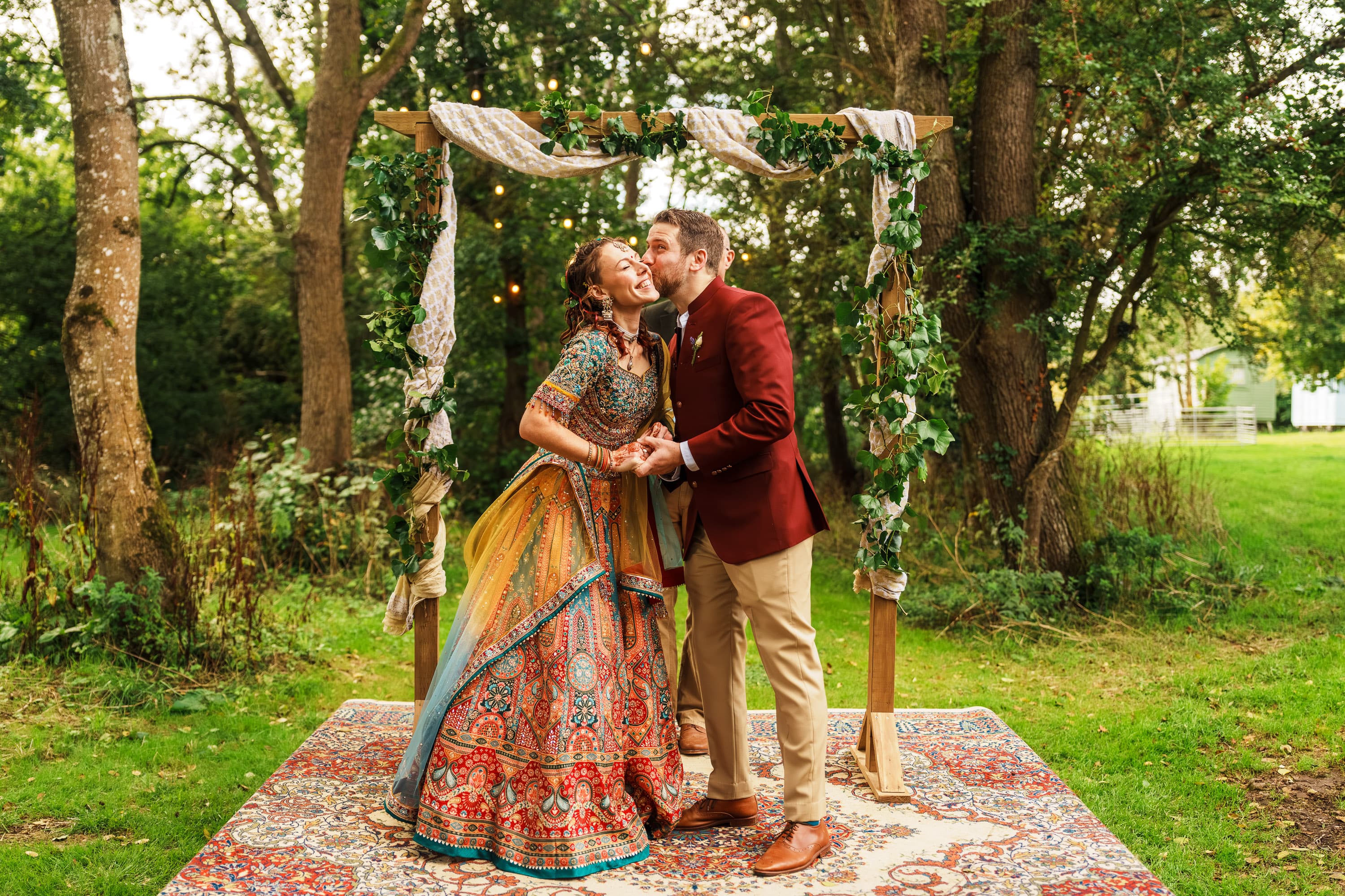 A wedding couple standing beneath an outdoor ceremony arch in soft daylight.